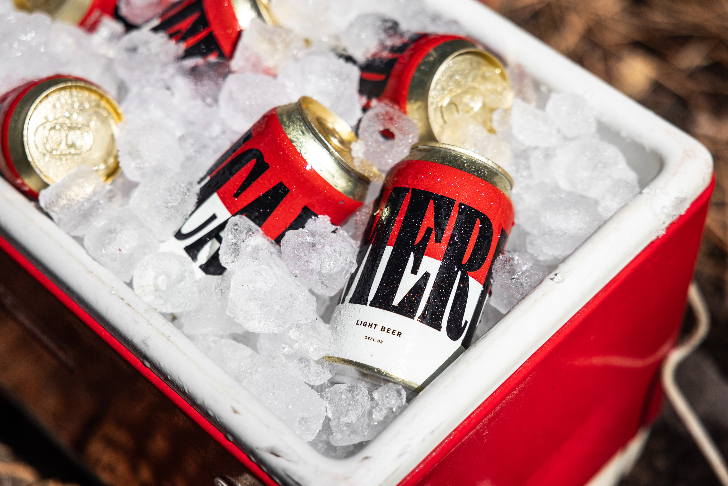 Several cans of Merican beer nestled among ice in a red cooler.
