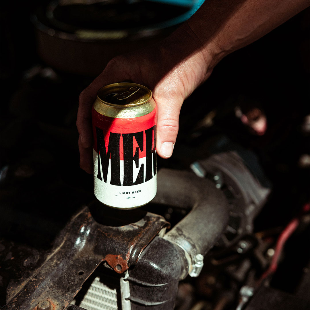 Merican beer can perched on the motor of an old car.