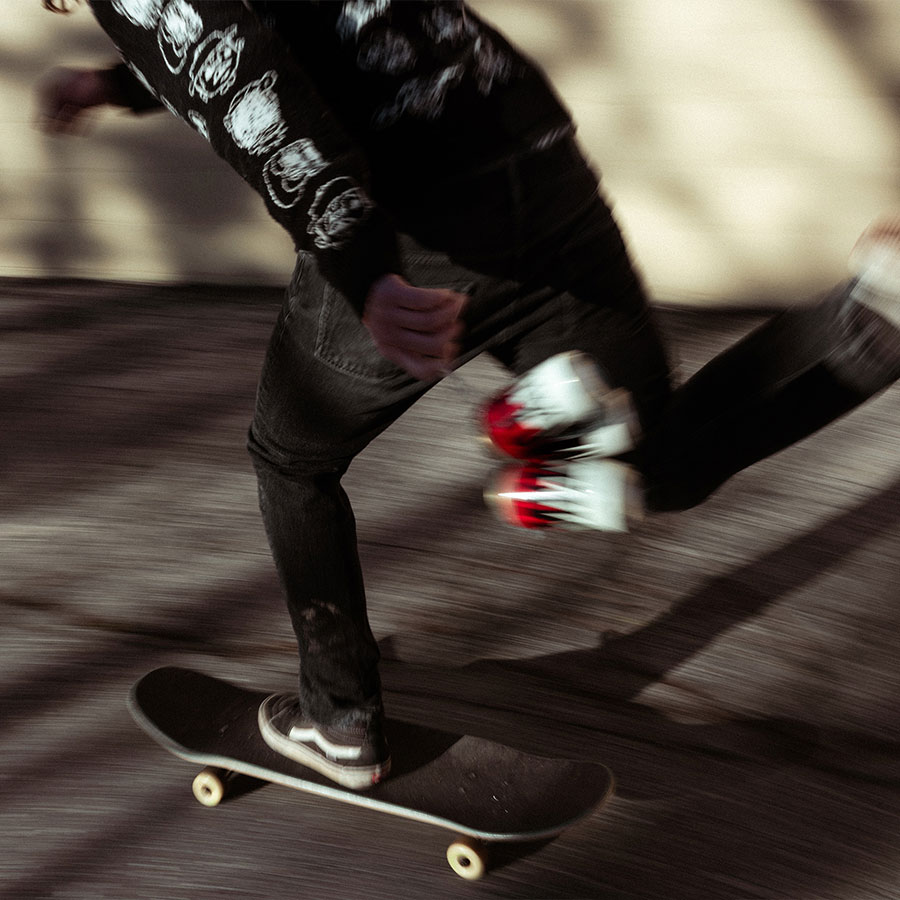 Motion-blurred image of someone on a skateboard holding a six-pack of Merican beers.